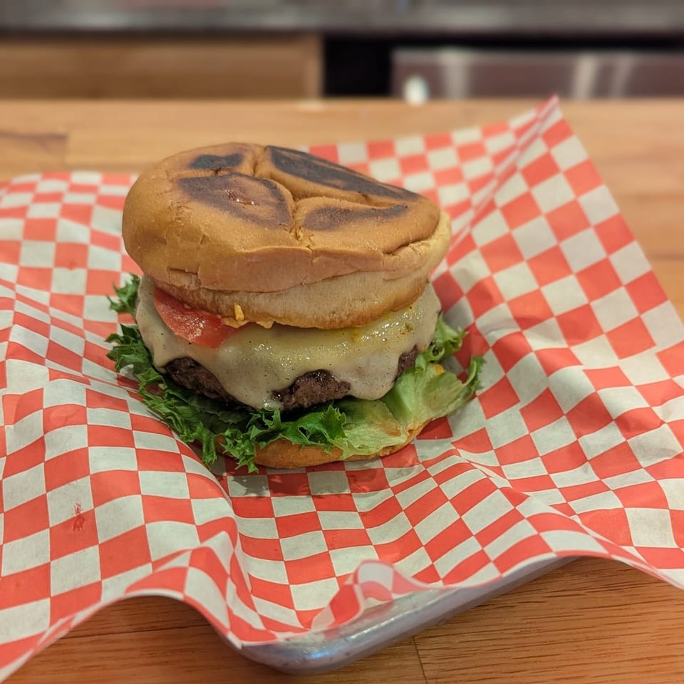 A Jaxon's Downtown burger with melted cheese, lettuce, and tomato on checkered paper.