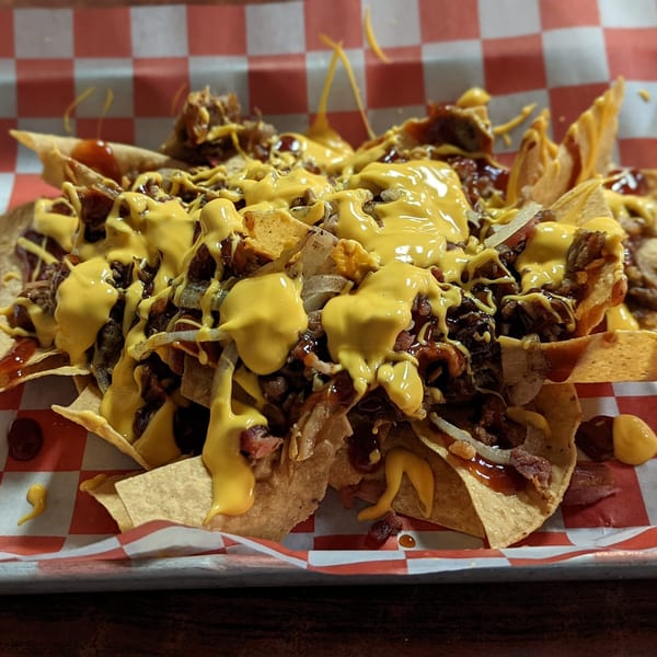 Jaxon's Downtown BBQ nachos, loaded with pulled pork, cheese sauce, and onions on a red checkered liner.