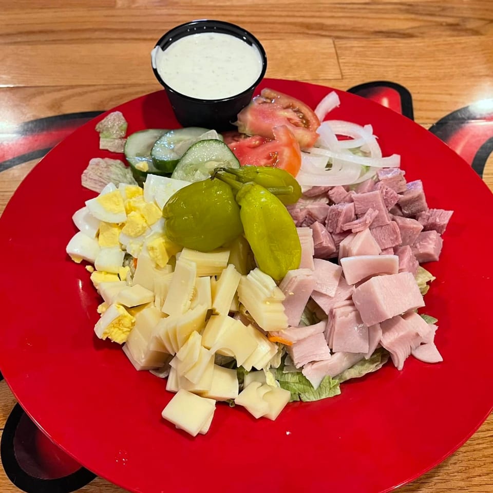 A vibrant Jaxon's Downtown chef salad with ham, cheese, eggs, and vegetables on a red plate.