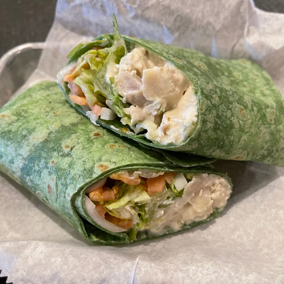 Two halves of a green tortilla wrap filled with chicken salad, lettuce, and carrots on white paper.
