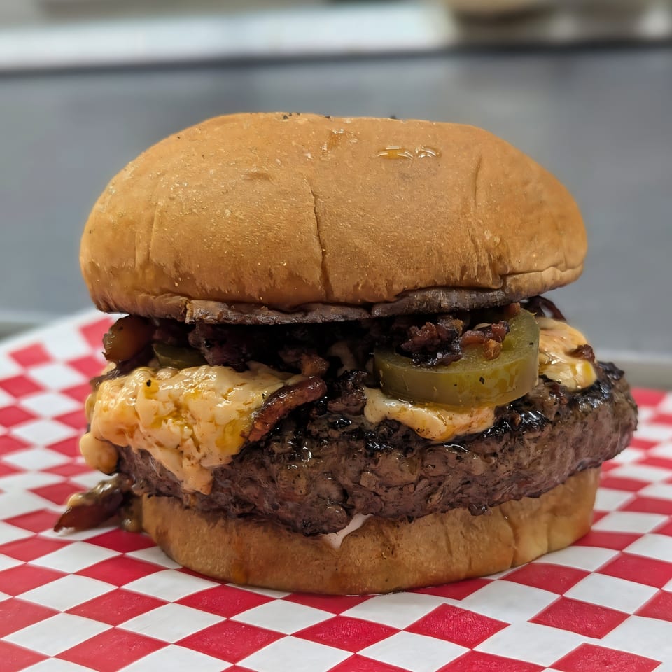 A Jaxon's Downtown burger with melted cheese, jalapeños, and caramelized onions on a red and white checkered paper.